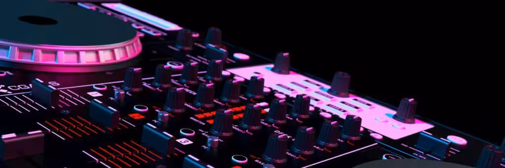 Nahaufnahme eines DJ-Mischpults mit verschiedenen Knöpfen und Schiebereglern, beleuchtet von rosa und blauen Lichtern vor einem dunklen Hintergrund – perfekt, um bei jedem Geburtstag oder jeder Firmenfeier für die richtige Stimmung zu sorgen.